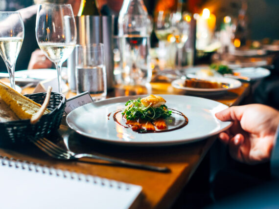 Photo of a full restaurant table, zoomed in on plate with entree, with note pad, fork and garlic bread basket nearby