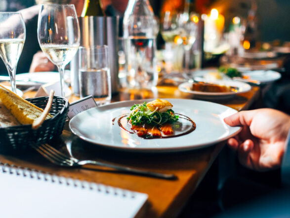 Photo of a full restaurant table, zoomed in on plate with entree, with note pad, fork and garlic bread basket nearby