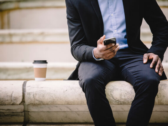 Man sitting on a step, looking at his phone, contemplating whether to answer.